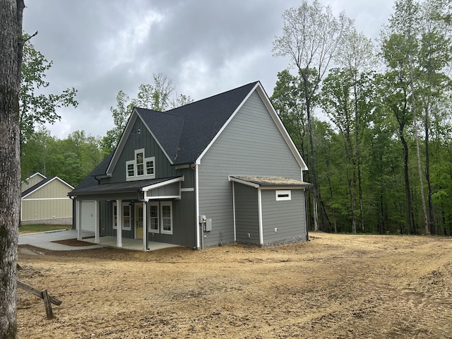 back of property with a porch, roof with shingles, and dirt driveway