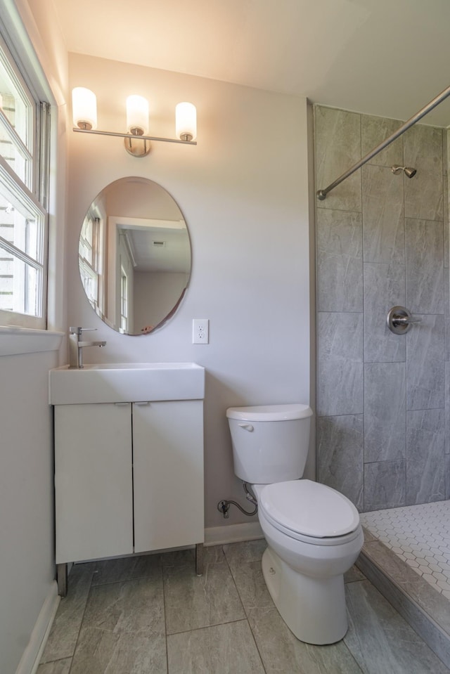 bathroom featuring a tile shower, vanity, toilet, and baseboards
