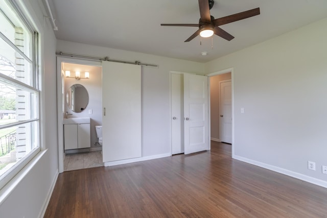 unfurnished bedroom featuring baseboards, ensuite bathroom, wood finished floors, and multiple windows