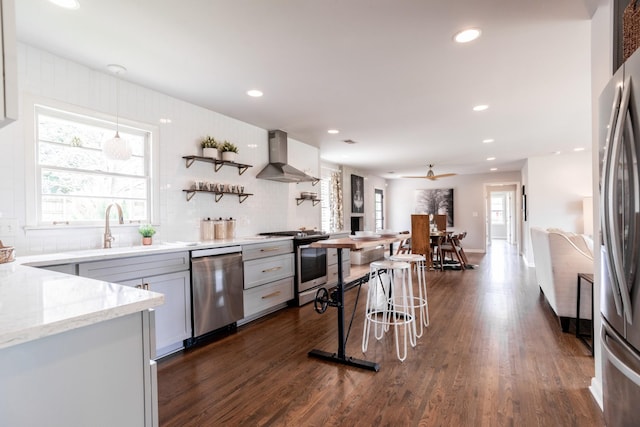 kitchen with wall chimney range hood, tasteful backsplash, a sink, dark wood finished floors, and appliances with stainless steel finishes
