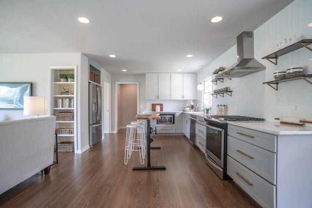 kitchen with open shelves, a sink, decorative backsplash, wall chimney exhaust hood, and appliances with stainless steel finishes