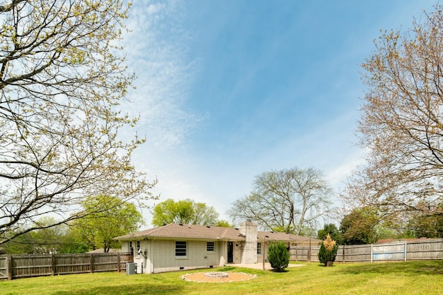 rear view of property with a fenced backyard, a chimney, brick siding, a yard, and crawl space