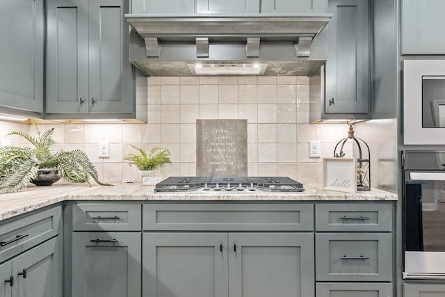 1111 Joe Martin Ln, Lebanon, TN 37087 - kitchen featuring stainless steel gas stovetop, wall chimney range hood, wall oven, decorative backsplash, and gray cabinetry