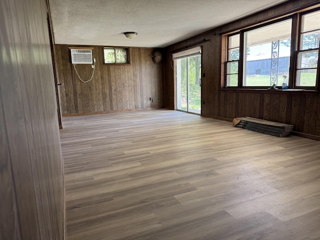 empty room with light wood-style floors, a textured ceiling, wood walls, and a wall unit AC