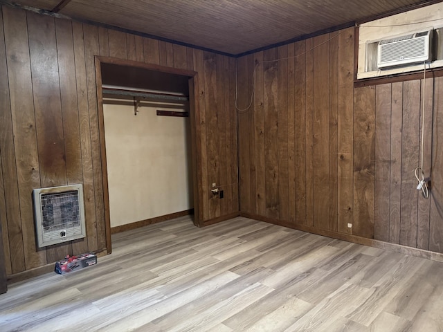 unfurnished bedroom with wooden walls, wood finished floors, a closet, and heating unit