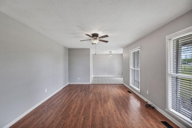 unfurnished room with a ceiling fan, wood finished floors, visible vents, and a textured ceiling
