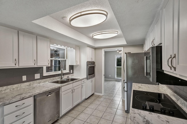kitchen featuring a sink, a tray ceiling, white cabinetry, baseboards, and appliances with stainless steel finishes