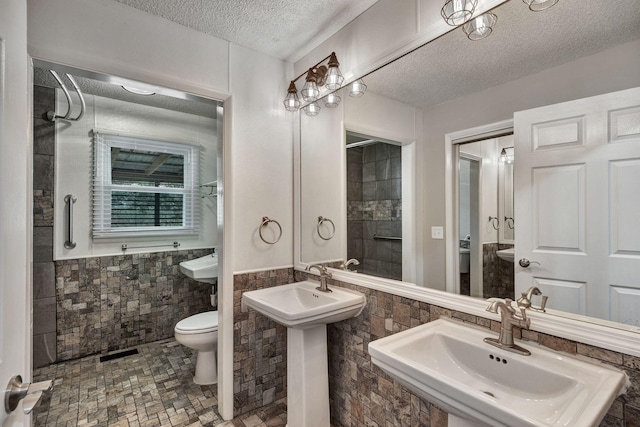 bathroom featuring a sink, a textured ceiling, tile walls, a wainscoted wall, and toilet