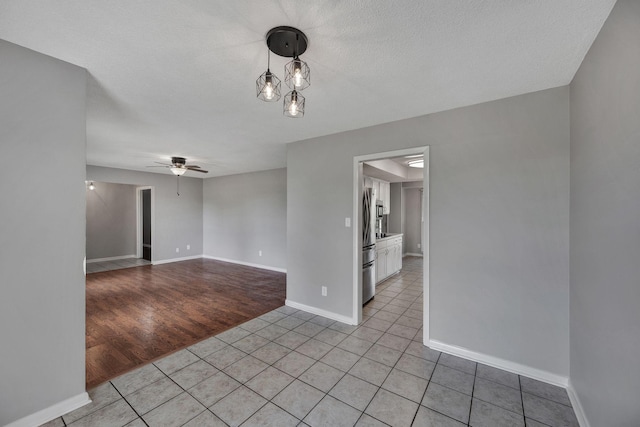 spare room with baseboards, a ceiling fan, a textured ceiling, and light tile patterned floors