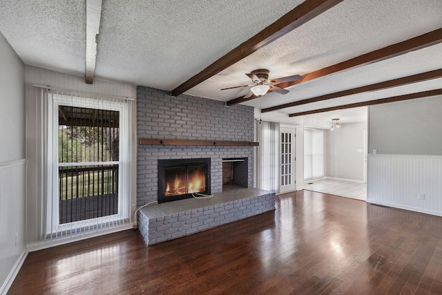 unfurnished living room featuring wood finished floors, a ceiling fan, beamed ceiling, a fireplace, and a textured ceiling