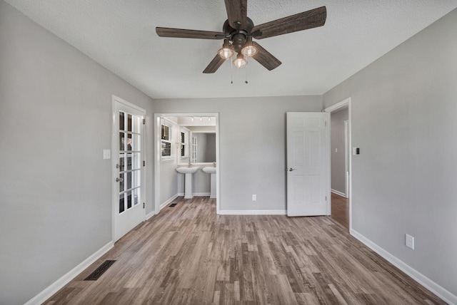 unfurnished bedroom featuring wood finished floors, visible vents, baseboards, and ensuite bathroom