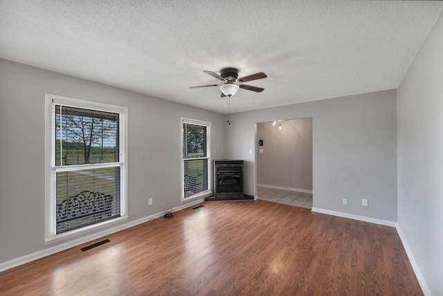 unfurnished living room featuring wood finished floors, visible vents, baseboards, a textured ceiling, and ceiling fan