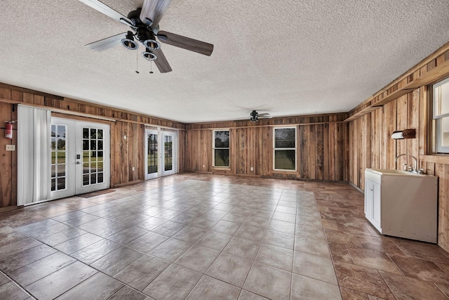 unfurnished living room with wooden walls, french doors, a textured ceiling, and a ceiling fan