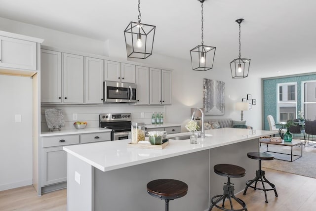 kitchen with light wood finished floors, stainless steel appliances, a sink, open floor plan, and a breakfast bar area
