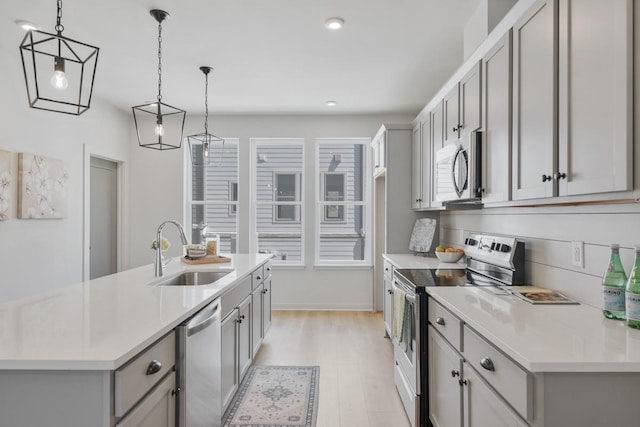 kitchen featuring a sink, light wood-type flooring, gray cabinets, light countertops, and appliances with stainless steel finishes