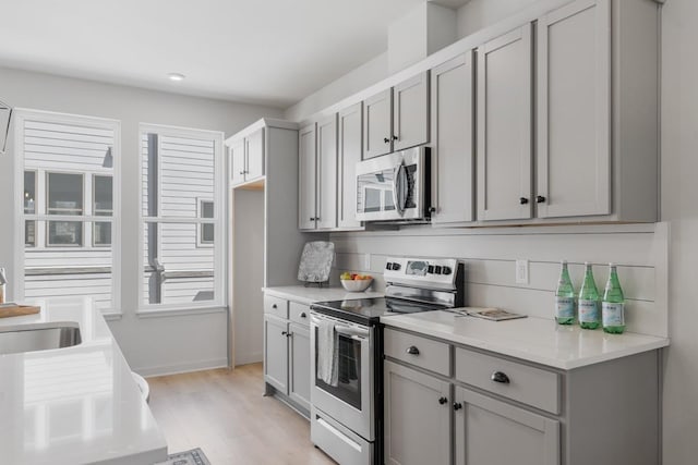 kitchen with light wood finished floors, a sink, gray cabinetry, light countertops, and appliances with stainless steel finishes