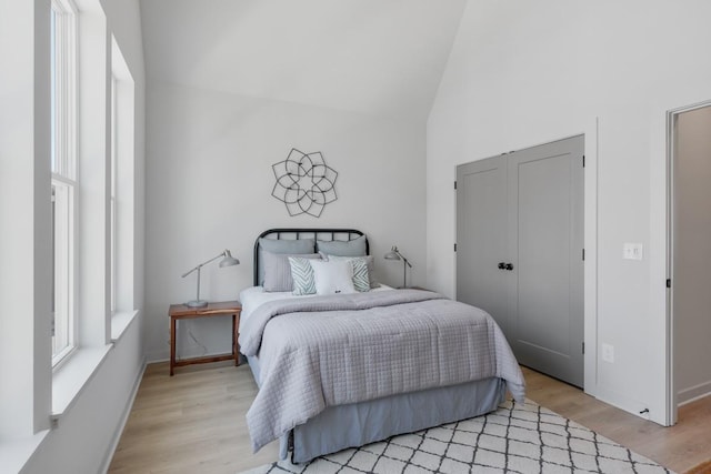 bedroom with light wood-type flooring, baseboards, high vaulted ceiling, and a closet