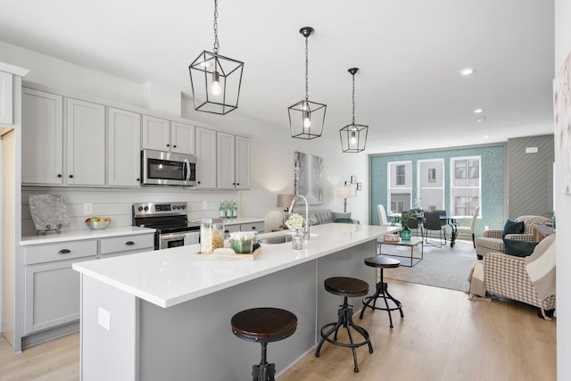 kitchen with a sink, open floor plan, a breakfast bar, light wood-type flooring, and appliances with stainless steel finishes