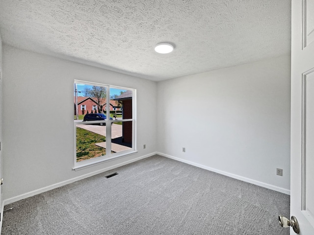 carpeted spare room with a textured ceiling, visible vents, and baseboards