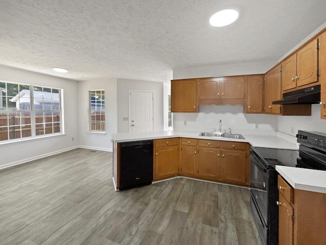 kitchen featuring a sink, black appliances, light countertops, a peninsula, and under cabinet range hood
