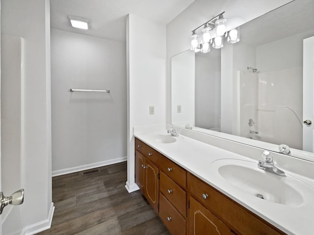 bathroom with wood finished floors, a sink, double vanity, baseboards, and shower / bathtub combination