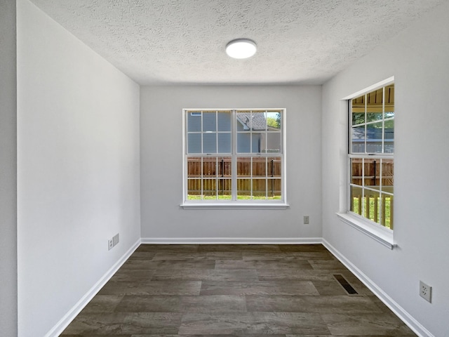 empty room with baseboards, visible vents, a textured ceiling, and dark wood-type flooring