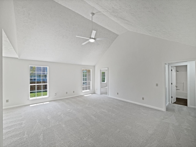 carpeted spare room with high vaulted ceiling, ceiling fan, baseboards, and a textured ceiling