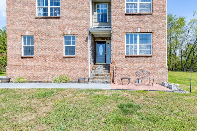 entrance to property featuring brick siding and a lawn