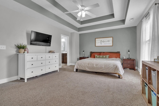 bedroom with connected bathroom, a tray ceiling, light colored carpet, baseboards, and visible vents