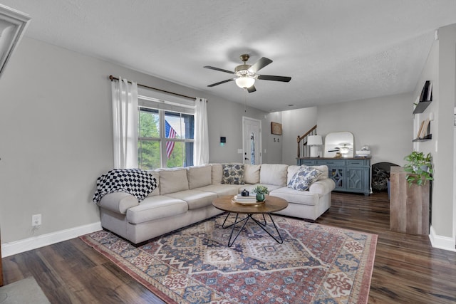 living area with stairs, a ceiling fan, baseboards, and dark wood-style flooring