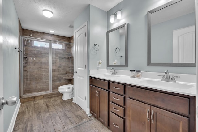 bathroom featuring a sink, a shower stall, double vanity, and toilet