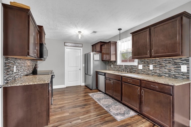 kitchen with stainless steel appliances, a sink, visible vents, dark brown cabinetry, and dark wood-type flooring