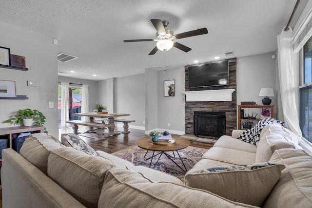 living area with a ceiling fan, a stone fireplace, wood finished floors, baseboards, and visible vents