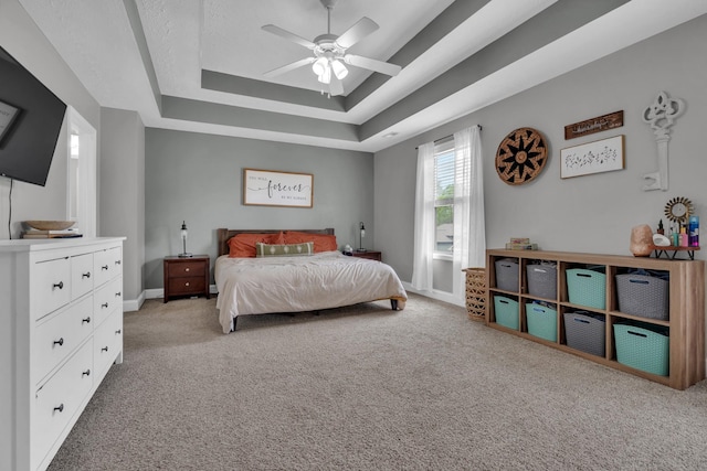 bedroom with light carpet, a ceiling fan, a tray ceiling, and baseboards