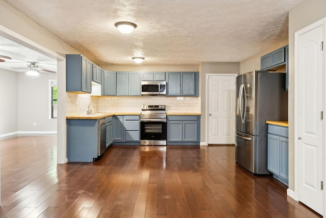 kitchen with a textured ceiling, decorative backsplash, stainless steel appliances, dark wood finished floors, and a ceiling fan