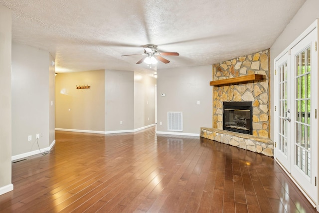 unfurnished living room featuring a fireplace, ceiling fan, visible vents, baseboards, and a textured ceiling