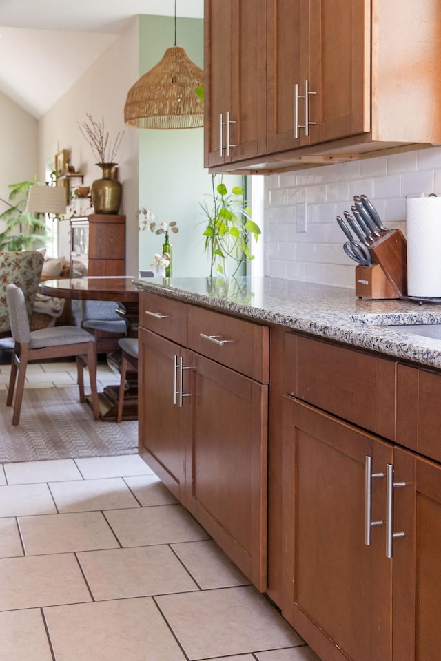 kitchen with brown cabinets, lofted ceiling, light stone counters, backsplash, and light tile patterned floors