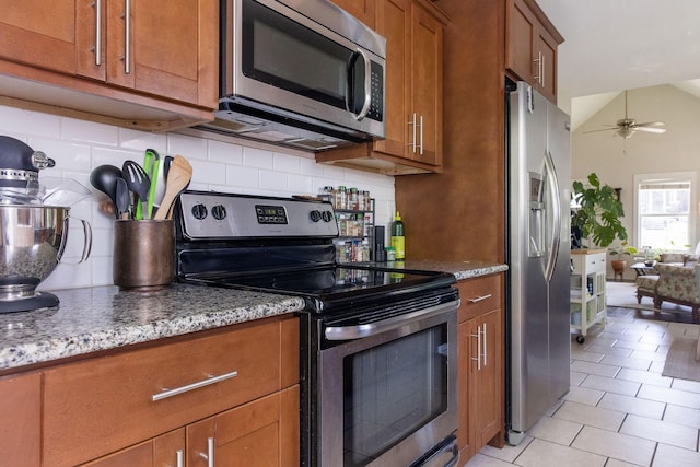 kitchen featuring brown cabinets, backsplash, appliances with stainless steel finishes, and light stone countertops