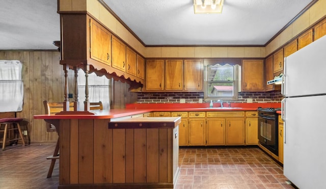 kitchen featuring a peninsula, freestanding refrigerator, black range oven, brown cabinets, and brick patterned floor