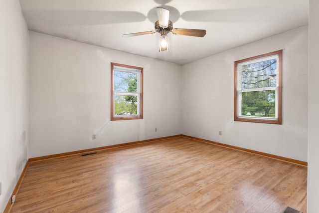 empty room with light wood-type flooring, visible vents, a ceiling fan, and baseboards