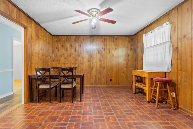 dining area with wood walls, a ceiling fan, and brick patterned floor