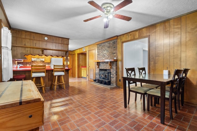 dining area featuring brick floor, a wood stove, wood walls, and a ceiling fan