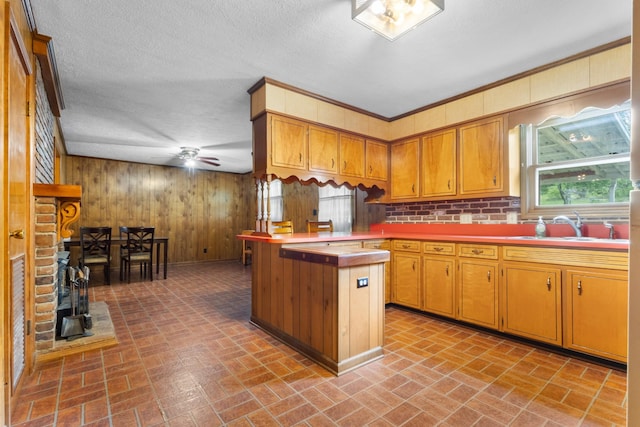 kitchen with wooden walls, a peninsula, a sink, and brick patterned floor