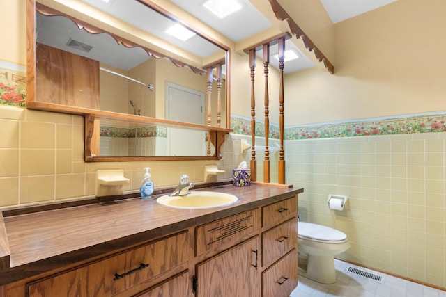 bathroom featuring toilet, tile walls, wainscoting, visible vents, and vanity