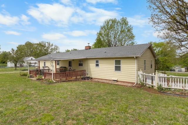 rear view of house featuring a chimney, a wooden deck, fence, and a yard