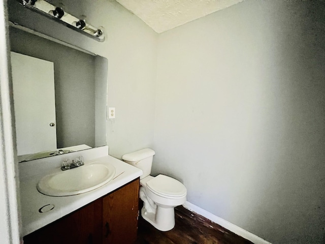 half bathroom featuring baseboards, toilet, vanity, and wood finished floors