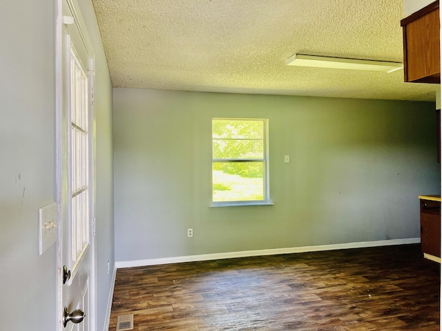 unfurnished room with a textured ceiling, wood finished floors, visible vents, and baseboards