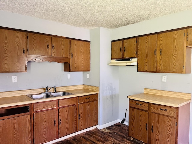 kitchen with light countertops, a textured ceiling, under cabinet range hood, and a sink