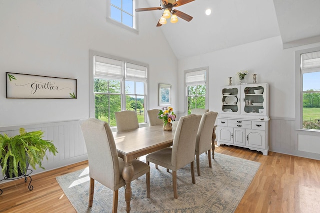 dining space with a ceiling fan, high vaulted ceiling, plenty of natural light, and a wainscoted wall