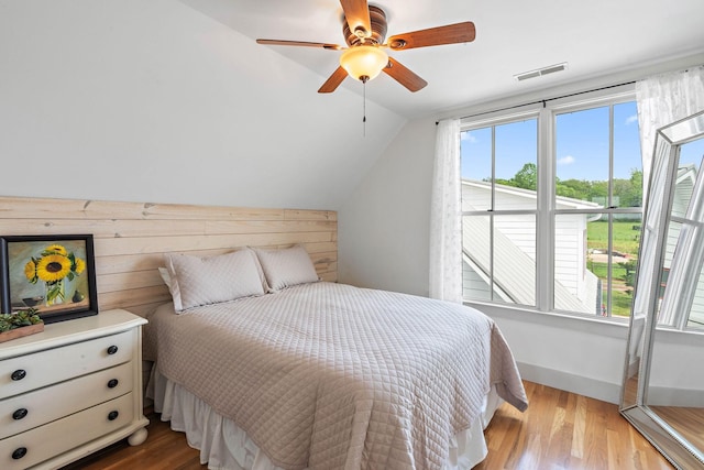 bedroom featuring wooden walls, ceiling fan, wood finished floors, lofted ceiling, and visible vents